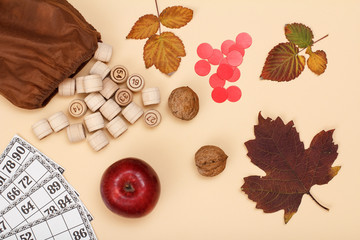 Wooden lotto barrels with bag, game cards, walnuts and apple on beige background. Autumn theme.