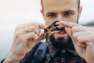 A cool picture of a man who holds a small crab in his arms while walking along the sea in cloudy cold weather