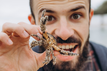 A cool picture of a man who holds a small crab in his arms while walking along the sea in cloudy cold weather
