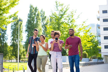 Cheerful friends using their phones for group video calls. Five people walking outside and using two smartphones, looking at screen, smiling and gesturing. Video connection concept
