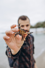 A cool picture of a man who holds a small crab in his arms while walking along the sea in cloudy cold weather