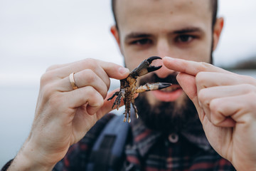 Portrait of a stylish bearded man with a small crab in his hands during the first tour of the sea