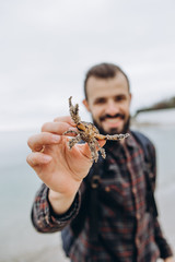 A cool picture of a man who holds a small crab in his arms while walking along the sea in cloudy cold weather