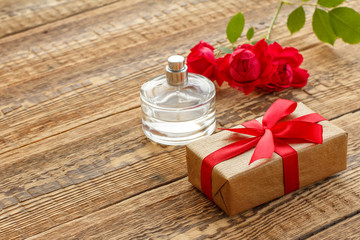 Gift box and bottle of perfume on wooden boards with flowers