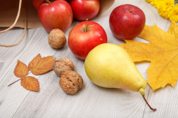 Ripe pear, walnuts and red apples with paper bag on wooden desk.