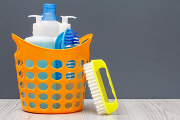 Bottles of dishwashing liquid in a basket with brush on wooden desk.