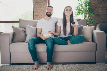 Obraz premium Adorable pair holding plate with popcorn changing channel search favorite show sitting sofa indoors
