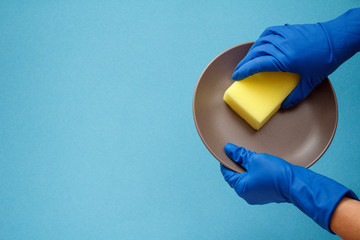 Women's hands in protective gloves with sponge and plate on blue background.