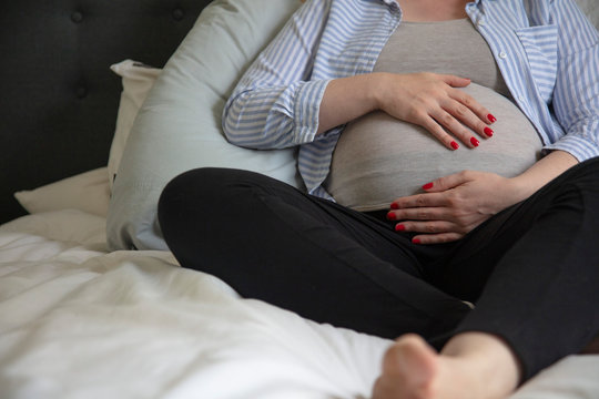 A young pregnant woman resting at home sitting on a bed. Expectant mother