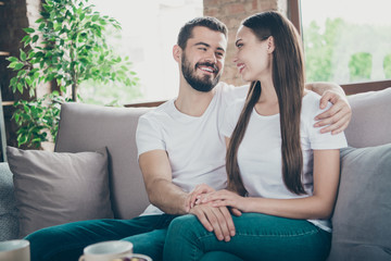 Photo of satisfied pair in love communicating sitting close to each other sofa indoors