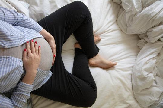 A young pregnant woman resting at home sitting on a bed. Expectant mother