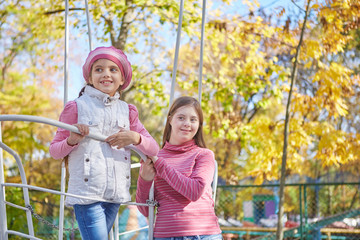 Girl with Down syndrome and little girl in autumn park.