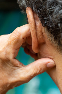 Senior woman putting index finger into her left ear, Grey curly hairs, Swimming pool background, Close up & Macro shot, Selective focus, Asian Body part, Healthcare concept, Symptom of hearing loss