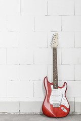 Fototapeta na wymiar Red electric guitar stands on the right against white brick wall