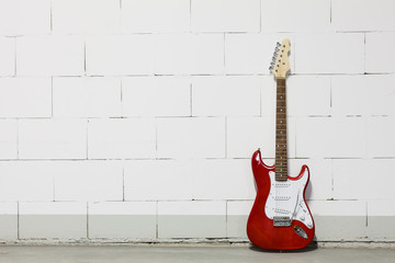 Red electric guitar stands to the right against white brick wall