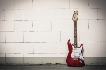 Fototapeta na wymiar Red electric guitar stands to the right against white brick wall, toned vignette crisp image