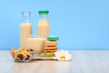 Bottles and glass of milk, bowl with muesli, macaroons on sackcloth.