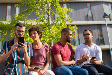 Happy peaceful people with phones sitting on parapet outside. Men and woman using smartphone, watching content and chatting. Leisure concept
