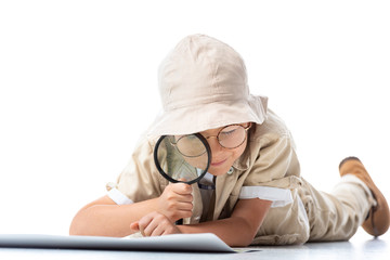 focused explorer child in hat and glasses looking at placard through magnifying glass on white