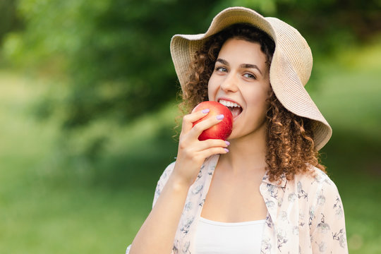 Beautiful girl in a hat eats an apple on nature