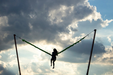 Girl jumping on an extreme swing. The girl flies launched by a rubber slingshot. The girl is experiencing adrenaline and joy from the jump. Woman on a background of clouds in flight.