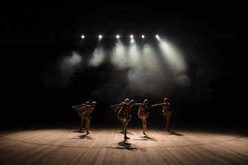 A group of small ballet dancers rehearses on stage with light and smoke