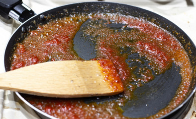 Red sauce made of dried tomatoes on frying pan. Wooden background, basil leaf and grains of pepper. Tomato is fried in a pan. Hot frying pan with tomato