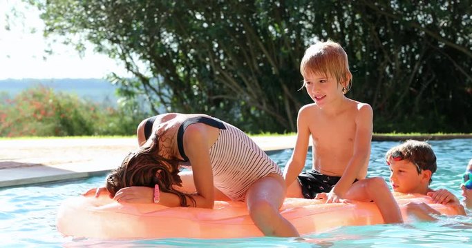 Kids on top of inflatable mattress having fun at the swimming pool
