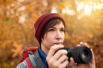 Attractive caucasian girl taking pictures with a mirrorless camera through the forest in the fall in Canada