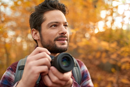 Attractive caucasian man taking pictures with a mirrorless camera through the forest in the fall in Canada