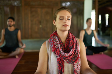 Woman giving meditation course to two multi-ethnic men on yoga mats in traditional temple in Bali Indonesia