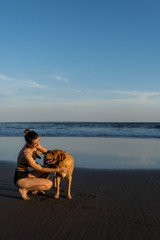 Happy young woman is enjoying sunset at the beach with her dog