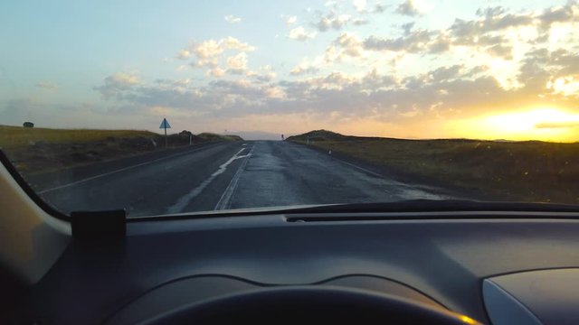 View from inside car on empty hilly road leading to horizon line at sunset or sunrise
