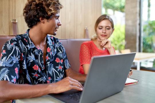 Candid Lifestyle Shot Of Multi-ethnic Man And Woman Millennials Collaborating And Smiling Together At Booth Of A Bright Modern Tropical Restaurant