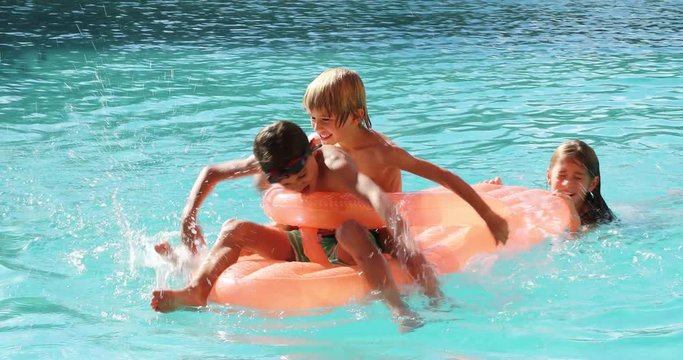 Kids playing the swimming pool water on top of inflatable mattress