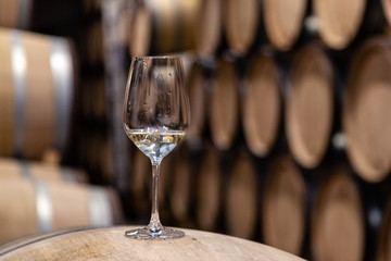 Closeup glass with white wine on background wooden wine oak barrels stacked in straight rows in...