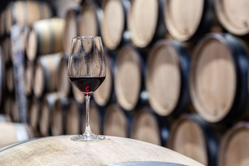 Closeup glass with red wine on background wooden wine oak barrel stacked in straight rows in order,...