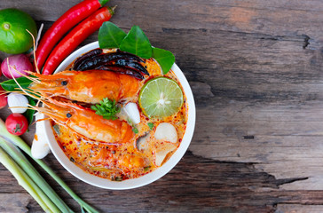 Tom Yum Goong or Shrimp soup spicy sour Soup Traditional food in Thailand contains chili, lime,lemongrass lime leaf, along with cooked rice in a white dish on the old wood background from top view.