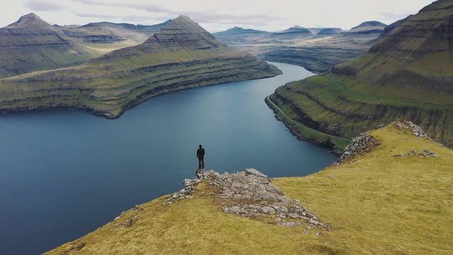 Flying around a hiker at the top of a mountain above Funningur on Faroe Islands