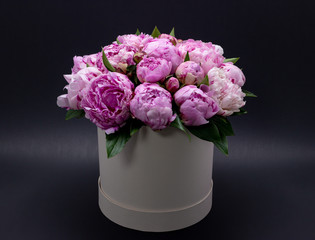Pink peonies in a hat box on a dark background.