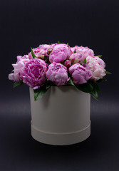 Pink peonies in a hat box on a dark background.