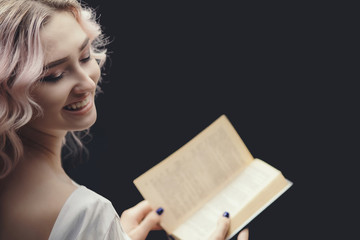 blonde happy girl holding open book, young beautiful woman reading a novel, concept of hobby, relaxation on black background