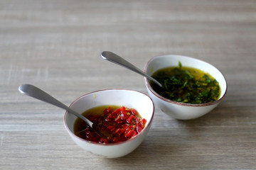 Two small bowls of olive oil sauce, one with chili pepper and one with basil. Selective focus.