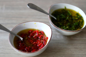 Two small bowls of olive oil sauce, one with chili pepper and one with basil. Selective focus.