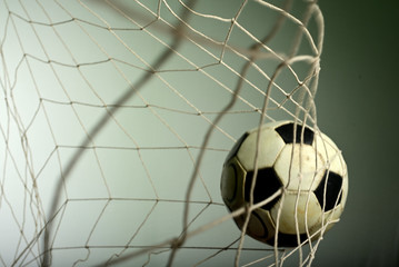 Scoring goal, Soccer ball in the net against gray background.