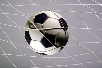 Scoring goal, Soccer ball in the net against gray background.