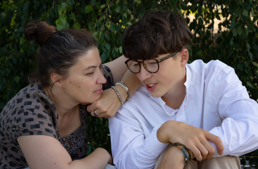 family relationships, middle-aged woman, mother, is talking with her student son. Young handsome man in a white shirt and glasses.