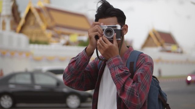 Attractive handsome tourist Asian man uses a film camera taking a photo of Wat Phra Kaew temple in Thailand. Asian man blogger happy enjoying leisure lifestyle travel.