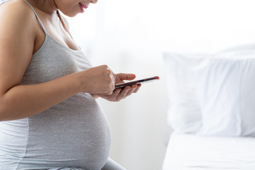 Happy pregnant woman with smartphone. Pregnancy, motherhood, technology, people and expectation concept.