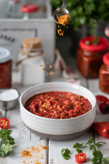 Process of cooking hot sauce of red hot peppers. Ingredients: pepper, greens, basil, paprika on a wooden table. Glass jars with ready-made sauce